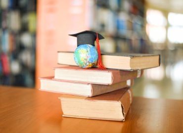 Books on the table in the library / Education learning old book stack and graduation cap on earth globe model on wood desk and blurred bookshelf room background